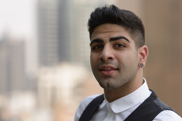 Portrait of young handsome Indian businessman against view of the city