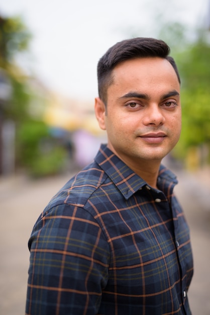 Portrait of young handsome Indian businessman in the streets outdoors