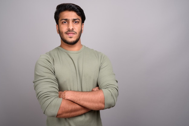 Portrait of young handsome Indian man against gray background