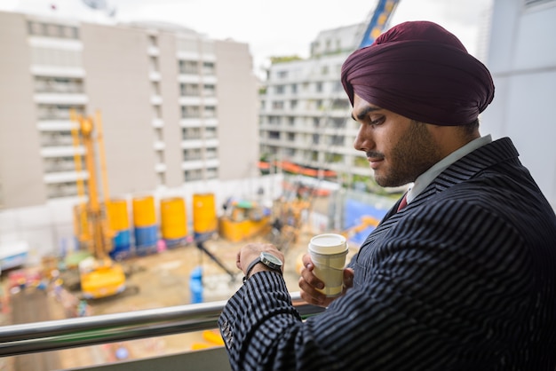 Portrait of young handsome Indian Sikh businessman wearing turban while exploring the city of Bangkok, Thailand