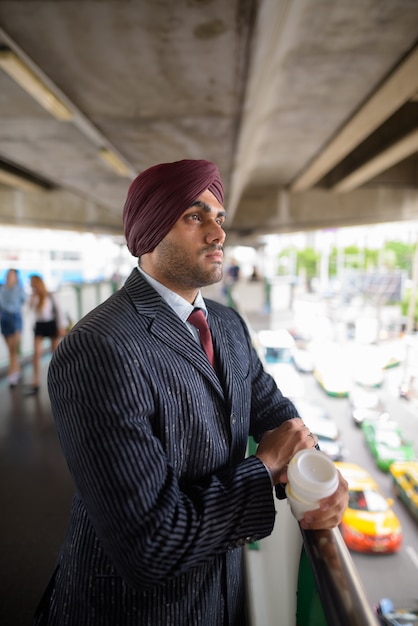 Portrait of young handsome Indian Sikh businessman wearing turban while exploring the city of Bangkok, Thailand