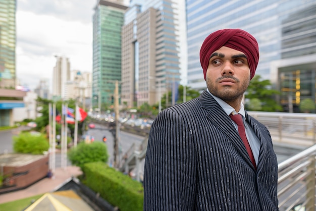 Portrait of young handsome Indian Sikh businessman wearing turban while exploring the city of Bangkok, Thailand