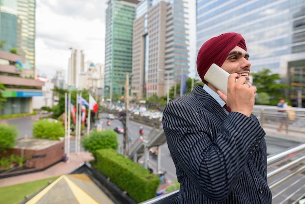 Portrait of young handsome Indian Sikh businessman wearing turban while exploring the city of Bangkok, Thailand