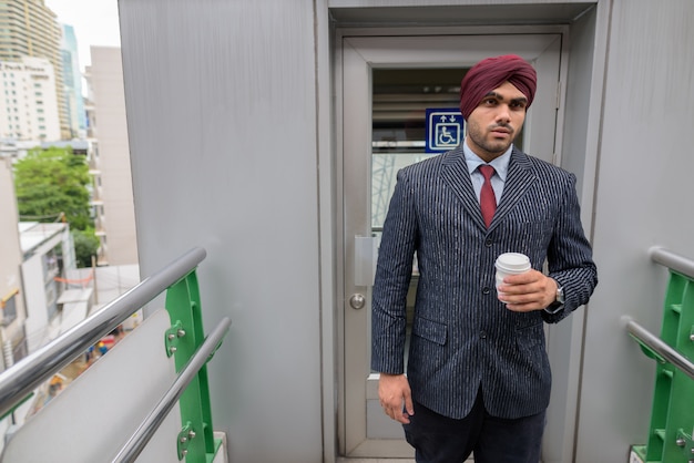 Portrait of young handsome Indian Sikh businessman wearing turban while exploring the city of Bangkok, Thailand