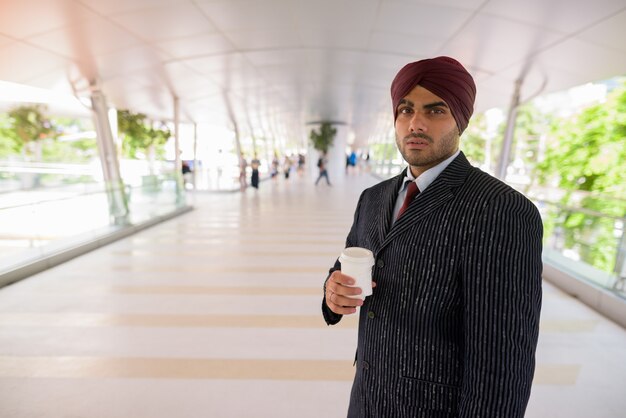 Portrait of young handsome Indian Sikh businessman wearing turban while exploring the city of Bangkok, Thailand