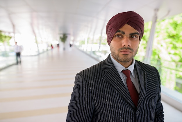 Portrait of young handsome Indian Sikh businessman wearing turban while exploring the city of Bangkok, Thailand