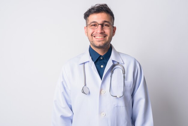 Portrait of young handsome Iranian man doctor with eyeglasses on white