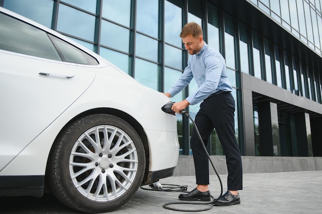 Ritratto di giovane uomo bello in abbigliamento casual in piedi presso la stazione di ricarica concetto di auto elettrica eco