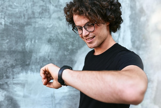 Portrait of young handsome man checking time on his wristwatch against gray concrete background Copy space for advertising text