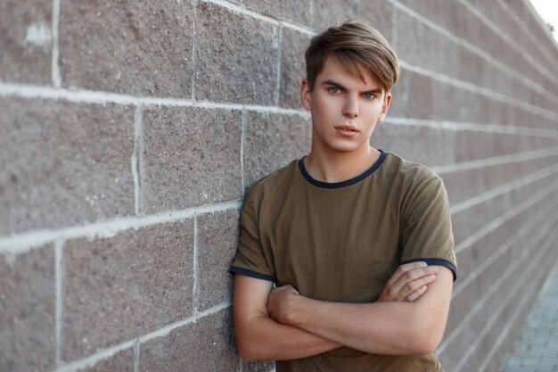 Portrait of a young handsome man in a classic T-shirt stands near a brick wall