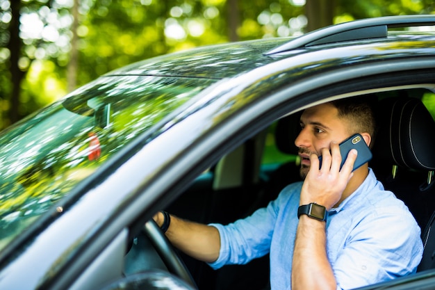 Portrait of young handsome man driving car and speaking on mobile phone