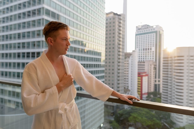 Portrait of young handsome man enjoying the view of the city from the balcony