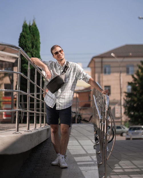 Portrait of young handsome man in glasses card shirt leaning on railing