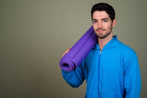 Portrait of young handsome man holding yoga mat ready for gym