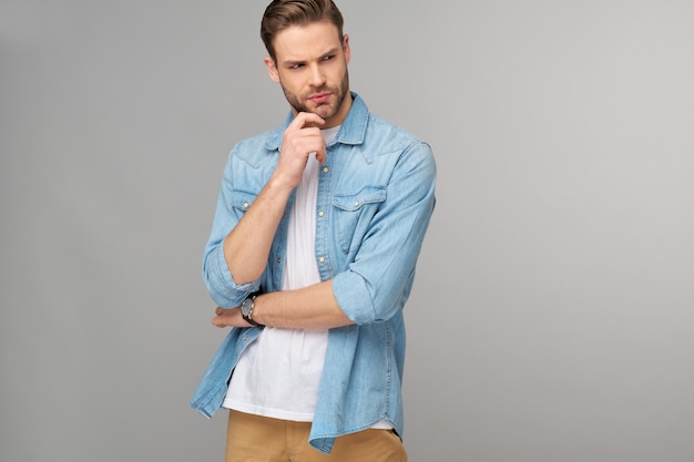 Portrait of young handsome man in jeans shirt over light wall