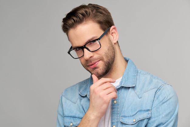 Ritratto di giovane uomo bello in camicia di jeans sopra la parete chiara