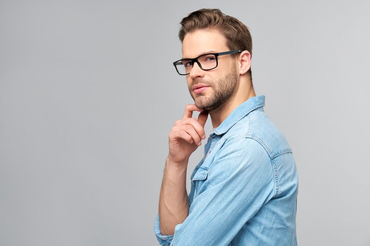 Portrait of young handsome man in jeans shirt over light wall