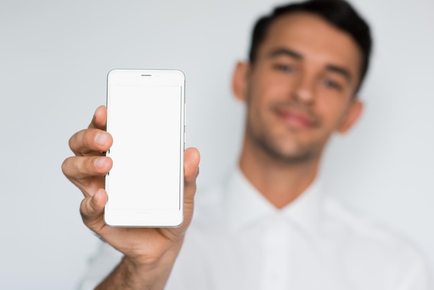 Portrait of young handsome man showing a blank smart phone screen isolated on a light gray background Blurred smile caucasian businessman with phone in studio