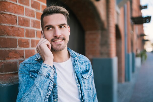 Portrait of young handsome man talking on the phone outdoors in the street. Communication concept.