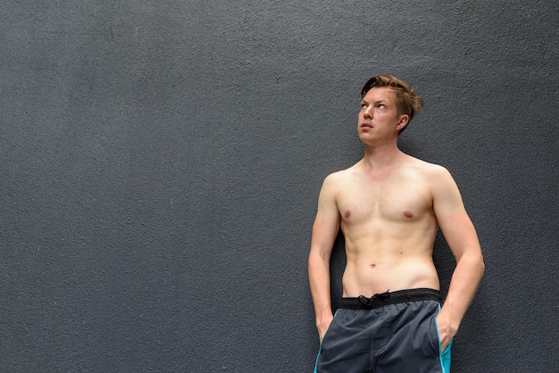 Photo portrait of young handsome man thinking while looking up against gray concrete wall