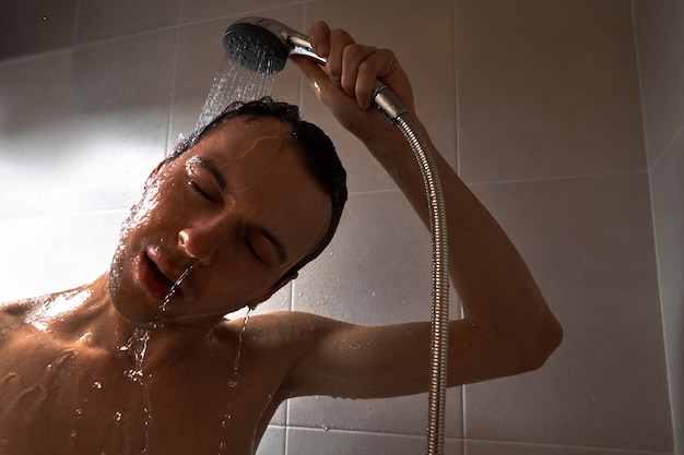 Portrait of young handsome man washes himself with shower gel, lathers head with shampoo in the bathroom at home close-up