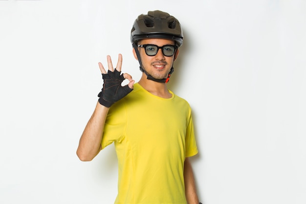 白い背景に親指を上げて大丈夫を示すサイクリストのヘルメットを身に着けている肖像画の若いハンサムな男