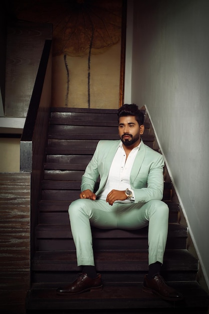 Портрет молодого красивого мужчины в строгом костюме сидит на лестнице в стильной позе