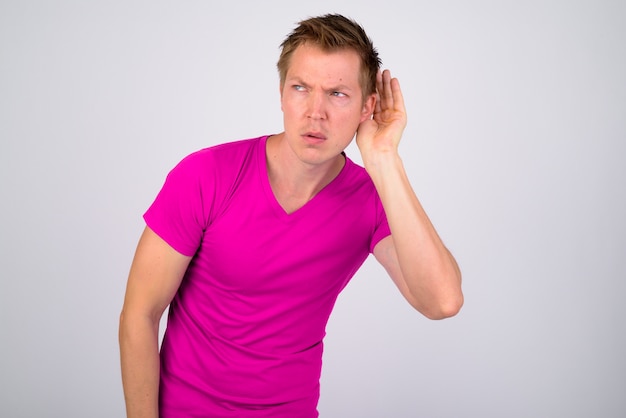 Portrait of young handsome man wearing purple shirt against white wall