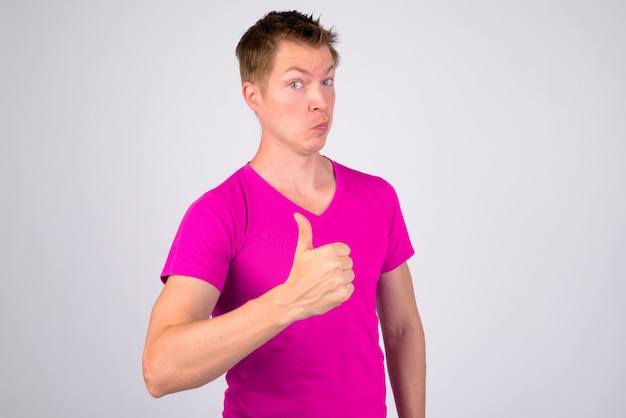 Portrait of young handsome man wearing purple shirt against white wall