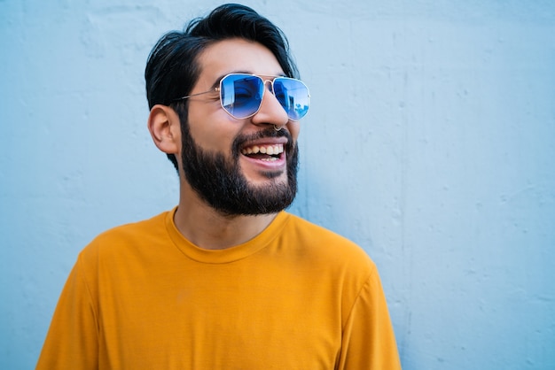 Portrait of young handsome man wearing summer clothes and sunglasses against blue background.