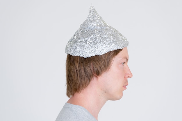 portrait of young handsome man wearing tin foil hat as conspiracy theory concept on white