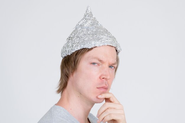 portrait of young handsome man wearing tin foil hat as conspiracy theory concept on white