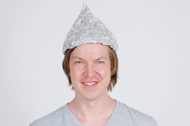 portrait of young handsome man wearing tin foil hat as conspiracy theory concept on white