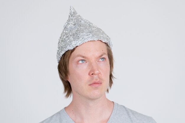 portrait of young handsome man wearing tin foil hat as conspiracy theory concept on white