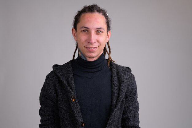 Portrait of young handsome man with dreadlocks against white wall