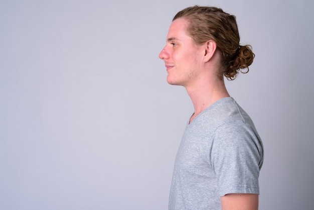 Portrait of young handsome man with hair tied against white wall