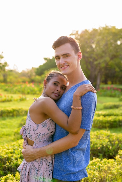 Portrait of young handsome man and young beautiful Asian woman relaxing together at the park