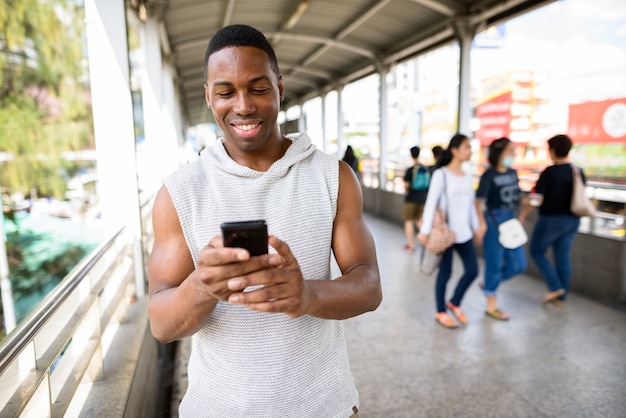 Portrait of young handsome muscular African man ready for gym at footbridge in the city