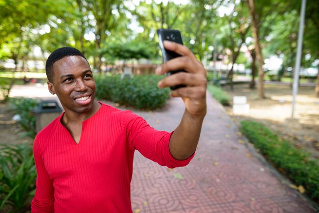 Portrait of young handsome muscular African man relaxing at the park outdoors