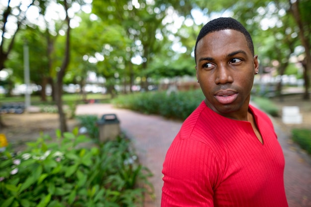 Portrait of young handsome muscular African man relaxing at the park outdoors