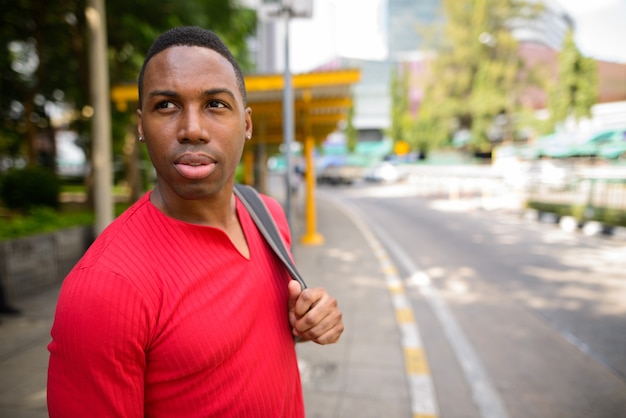 Portrait of young handsome muscular African man waiting at the bus stop