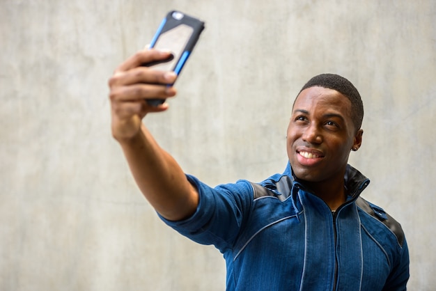 Portrait of young handsome muscular African man wearing blue jacket against concrete wall outdoors