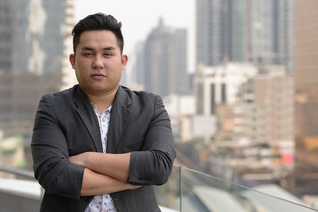 Portrait of young handsome overweight Filipino businessman in suit against view of the city