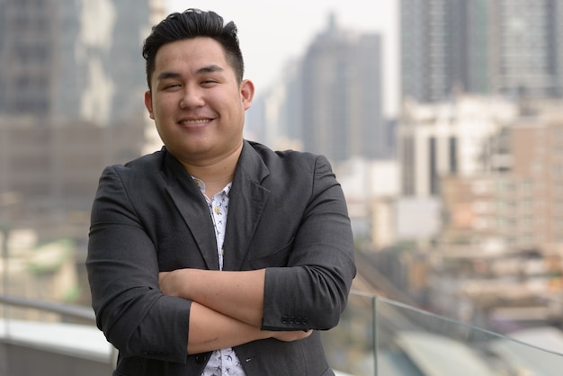 Portrait of young handsome overweight Filipino businessman in suit against view of the city