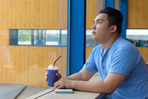 Portrait of young handsome overweight Filipino man relaxing at the coffee shop