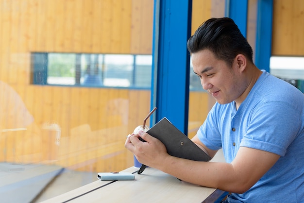 Portrait of young handsome overweight Filipino man relaxing at the coffee shop