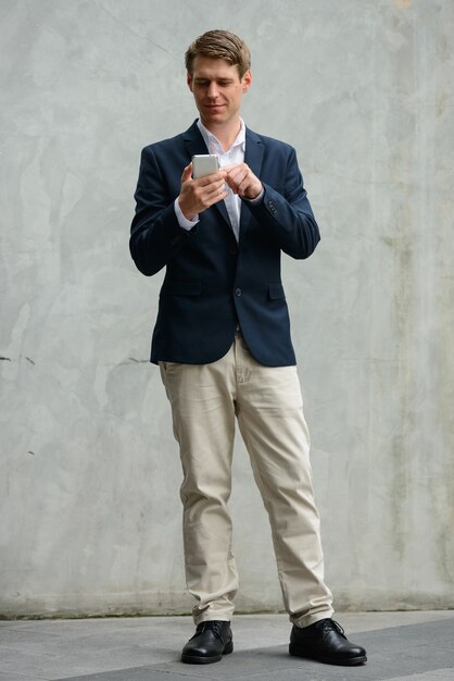 Portrait of young handsome Scandinavian businessman with blond hair on concrete wall