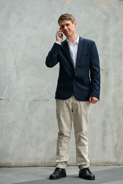 Portrait of young handsome Scandinavian businessman with blond hair on concrete wall