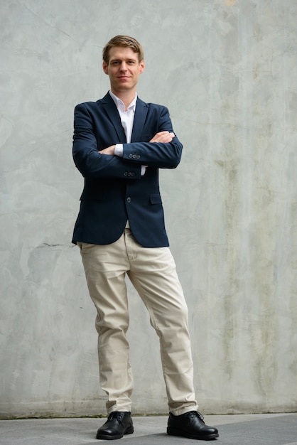 Portrait of young handsome Scandinavian businessman with blond hair on concrete wall