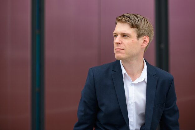 Portrait of young handsome Scandinavian businessman with blond hair on concrete wall